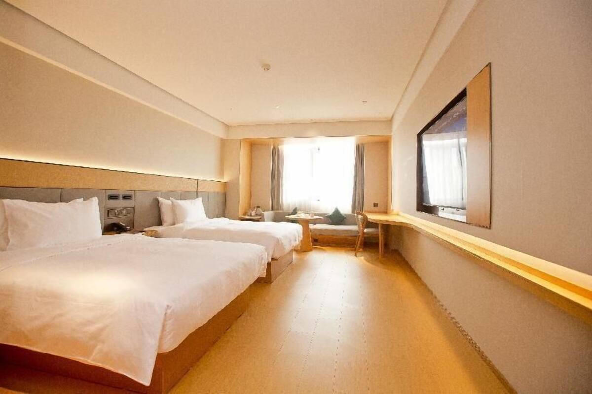 A hotel room with two beds, a desk, a chair, and a large window.