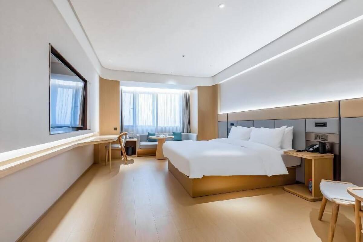 A modern hotel room with a large bed, a desk, a chair, and a small table.