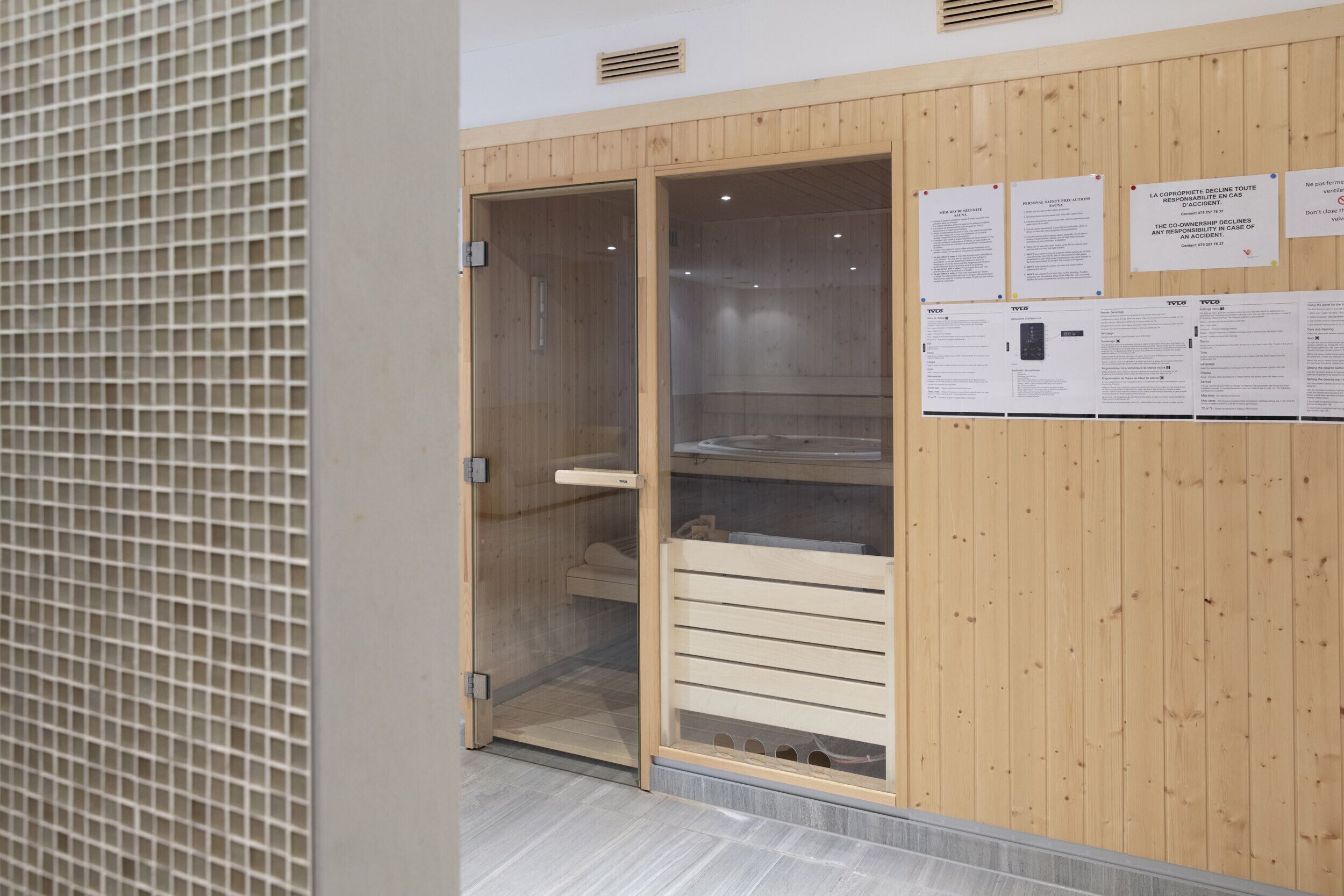 Een sauna met houten wanden en een glazen deur, met een bank en bedieningspaneel.