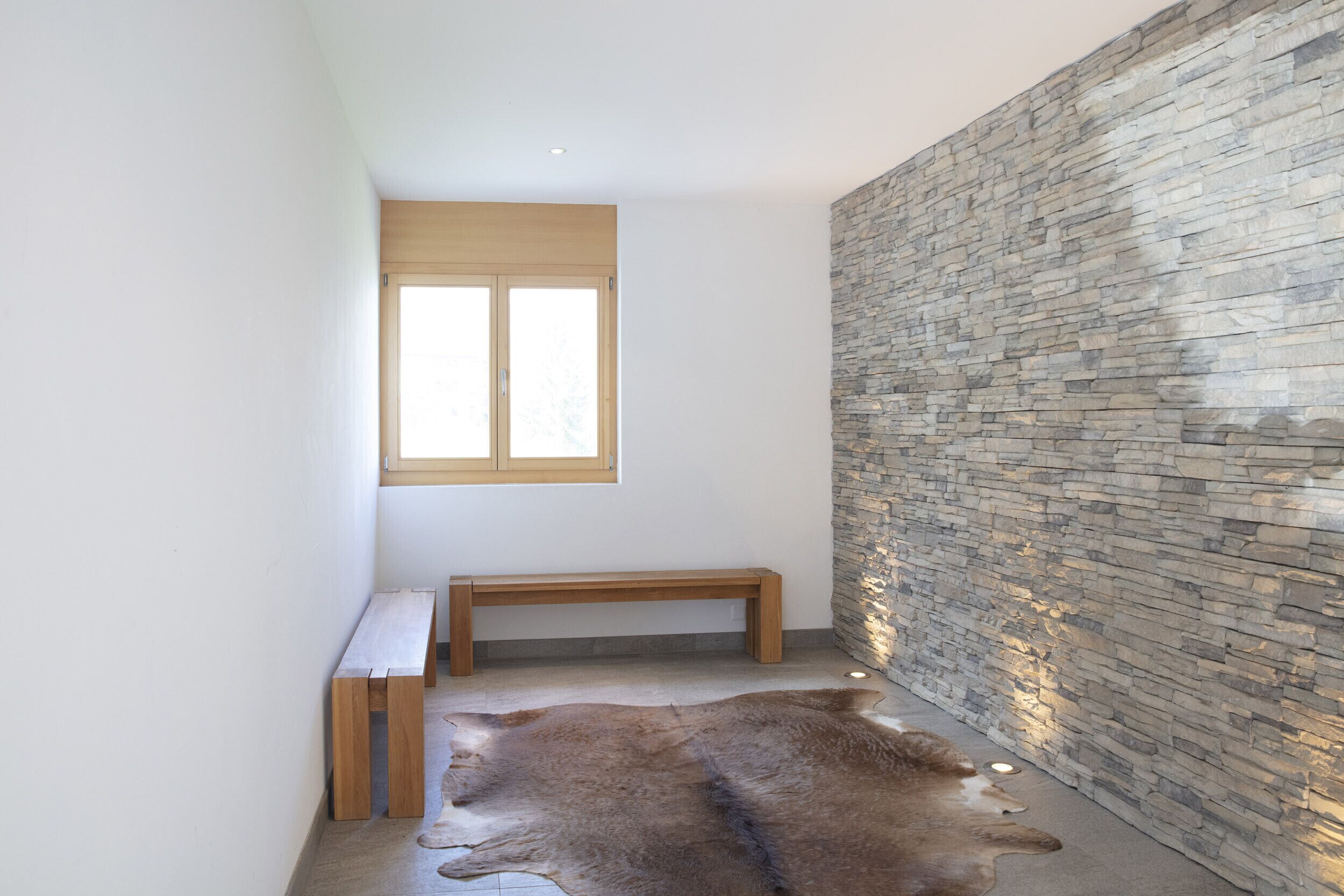 Ein Zimmer mit einer Steinwand, einer Holzbank und einem Fellteppich.