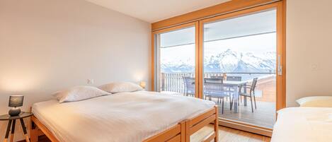 A bedroom with a large bed, a bedside table with a lamp, and a view of mountains through a sliding glass door.