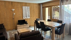 Ein modernes Wohnzimmer mit einer Holzwand, einem Esstisch mit Stühlen, einer Couch, einem Fernseher und einer Stehlampe.