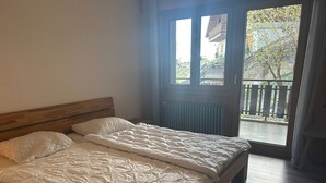 Ein Schlafzimmer mit einem Holzbett, einem Heizkörper und Blick auf einen Balkon mit Zaun und Bäumen.