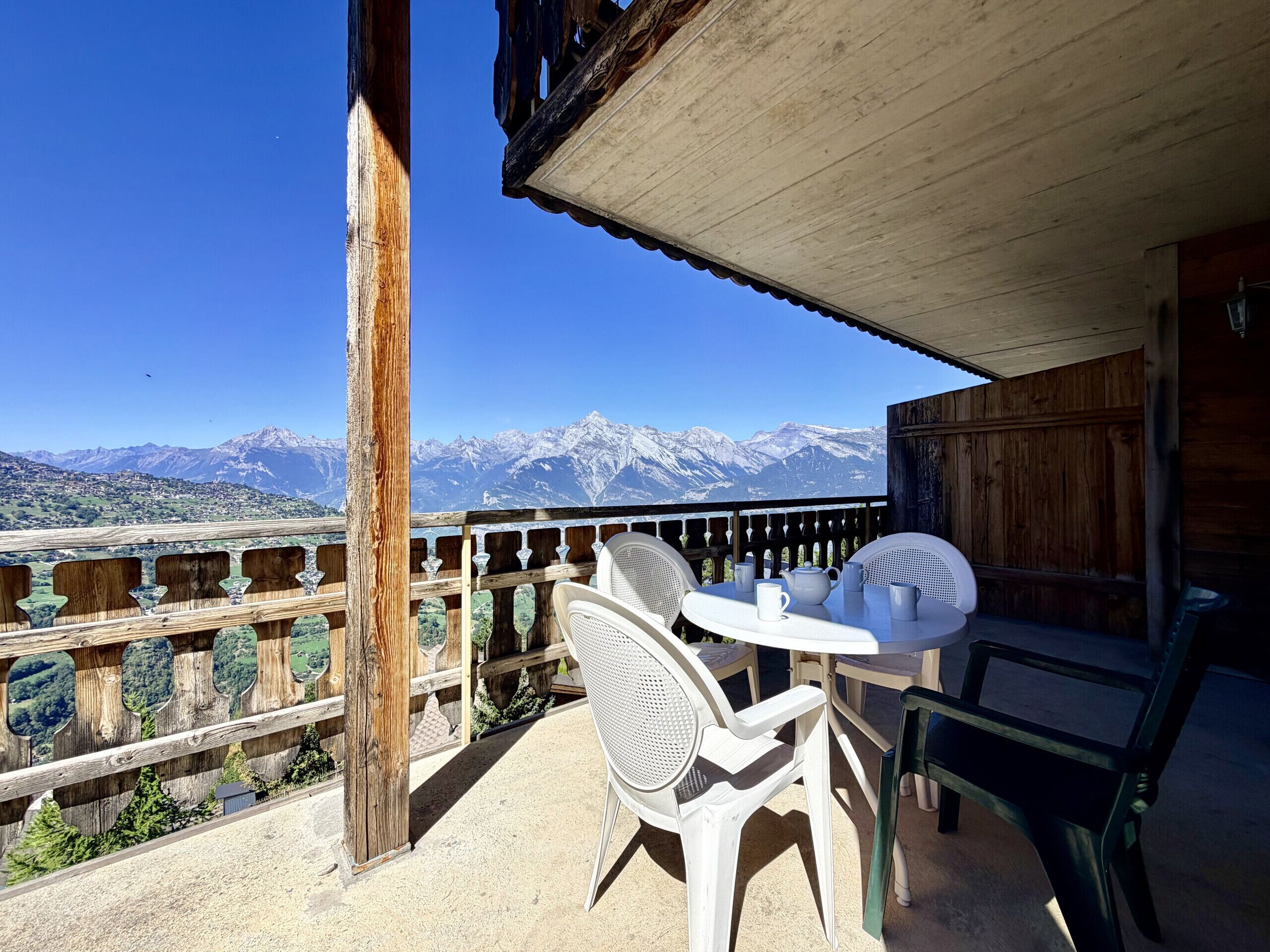 A balcony with a table and chairs, overlooking a mountainous landscape.