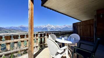 Een balkon met een tafel en stoelen, met uitzicht op een bergachtig landschap.