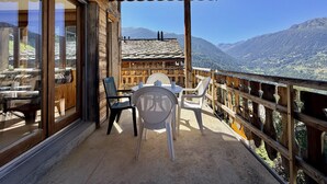 Un balcón con mesa y sillas, con vista a un paisaje montañoso.