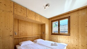 Una habitación de madera con dos camas, una ventana con vista a la montaña y una estantería con un hervidor.