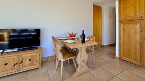A dining area with a wooden table, chairs, a television on a cabinet, and a wine bottle.
