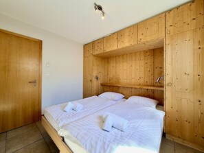 A bedroom with a wooden wardrobe, a bed with white bedding, and a ceiling light.