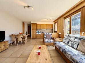 Una sala de estar acogedora con un sofá, una mesa de centro de madera y un comedor con sillas y un televisor.