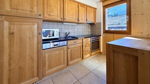 A kitchen with wooden cabinets, a microwave, a stove, and a window with a view of a snowy landscape.