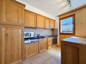 Una cocina con armarios de madera, microondas, estufa y ventana con vistas a un paisaje nevado.