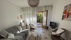 Un salon avec un canapé, des fauteuils, un téléviseur et une vue sur la verdure à l’extérieur.