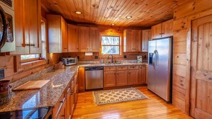 A spacious kitchen with wooden cabinets, granite countertops, a stainless steel refrigerator, and a dishwasher. - Mountain Lodge Near Downtown (Boone)