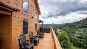 A wooden cabin with a deck, black Adirondack chairs, and a view of a forested valley. - Mountain Lodge Near Downtown (Boone)