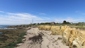 Un paisaje costero con una playa arenosa, acantilados rocosos y casas al fondo.