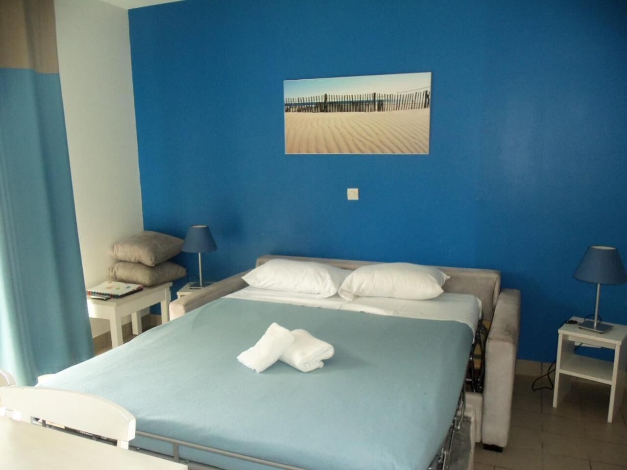Habitación de hotel con cama, escritorio, silla, lámpara y un cuadro en la pared.