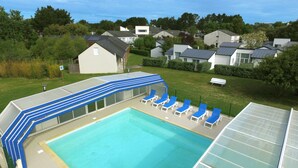Una piscina con sillas reclinables azules y una zona cubierta.