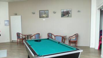 Une table de billard dans une pièce où se trouvent quatre chaises, un radiateur et deux tableaux encadrés au mur.