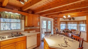 A wooden cabin-style kitchen with a central island, wooden cabinets, and a dining area with a table and chairs. - Quaint Log Cabin in Great Location (Banner Elk)