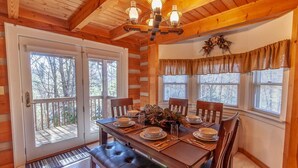 A wooden dining room with a table set for four, a chandelier, and a view through the glass doors. - Quaint Log Cabin in Great Location (Banner Elk)