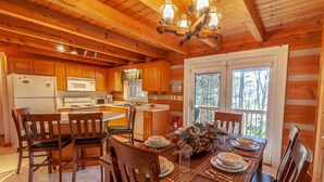 A cozy cabin-style kitchen with wooden cabinets, a central island, and a dining area set for four. - Quaint Log Cabin in Great Location (Banner Elk)