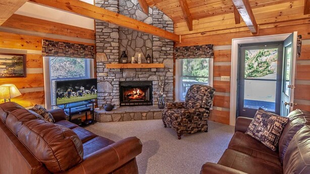 A cozy cabin interior with a stone fireplace, leather sofas, a television, and a wooden ceiling. - Quaint Log Cabin in Great Location (Banner Elk)