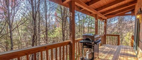 A wooden deck with a grill, surrounded by trees.