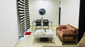 A living room with a sofa, a coffee table, a dining table with chairs, a ceiling fan, and a patterned curtain.