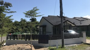 A residential house with a tiled roof, a fenced yard, and a parked car.