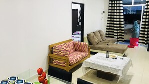 A living room with a sofa, a coffee table, and a chair. There is a window with curtains and a view of the outside.