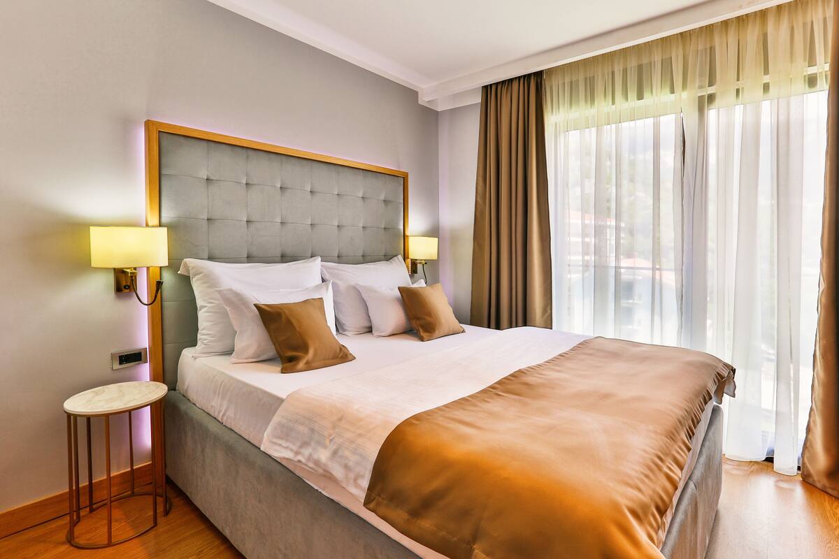 A hotel room with a large bed, two bedside lamps, a small table, and a window with curtains.