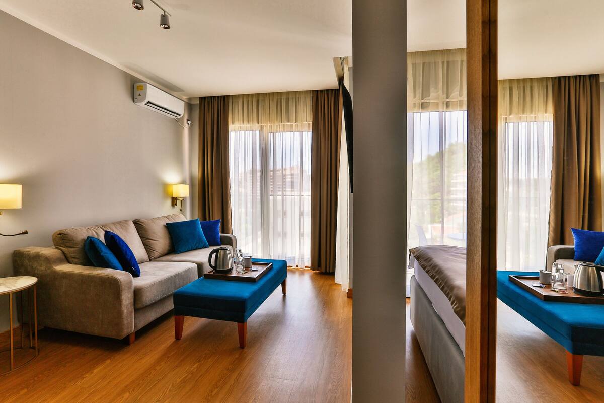 A hotel room with a sofa, a coffee table, a bed, and a window with curtains.