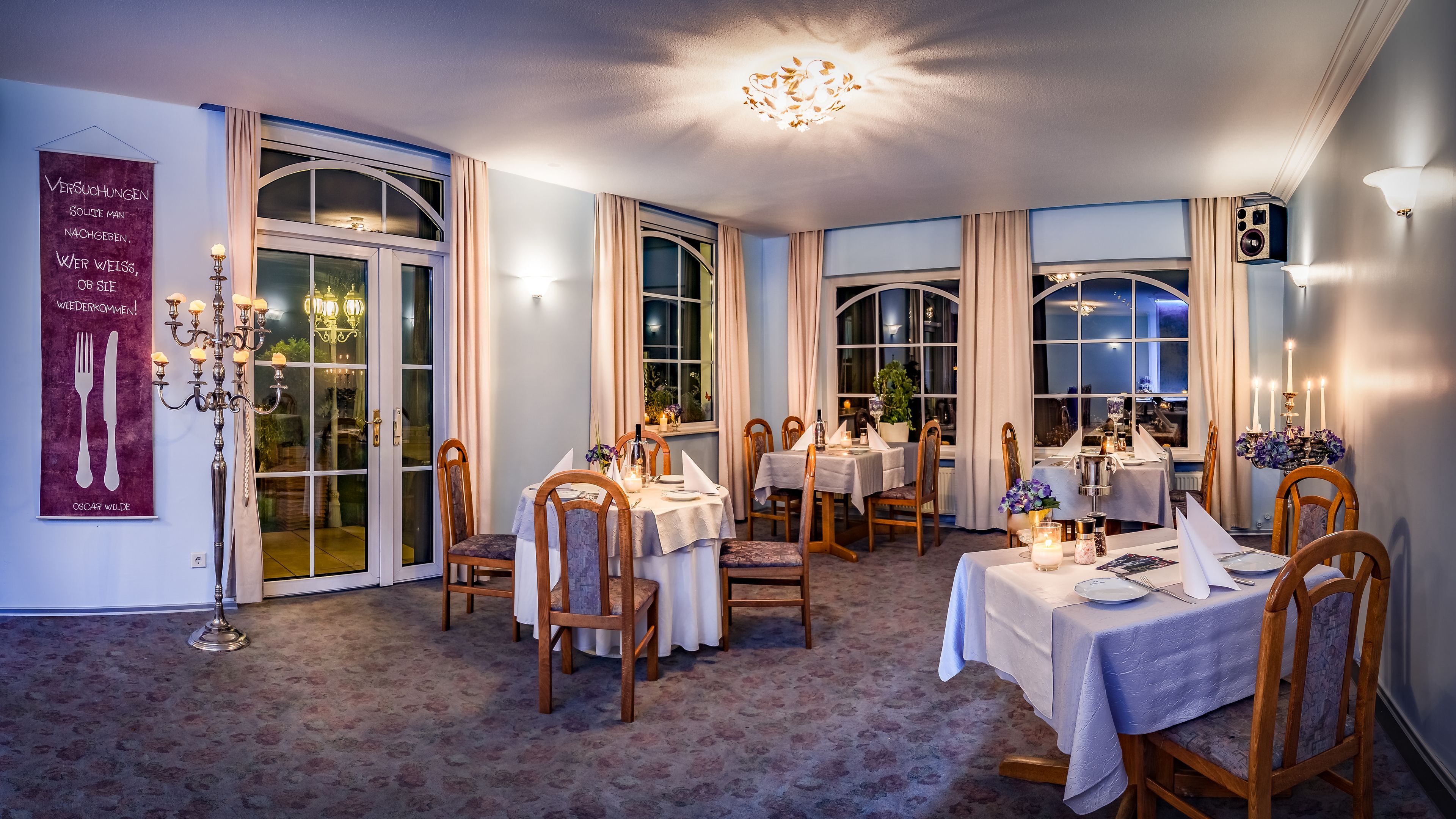 A dining area with multiple tables, chairs, and a chandelier.