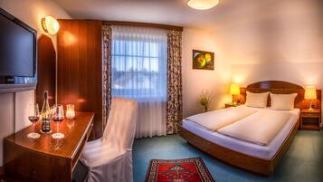 A hotel room with a bed, bedside tables, a TV, a desk with a chair, and a window with curtains.