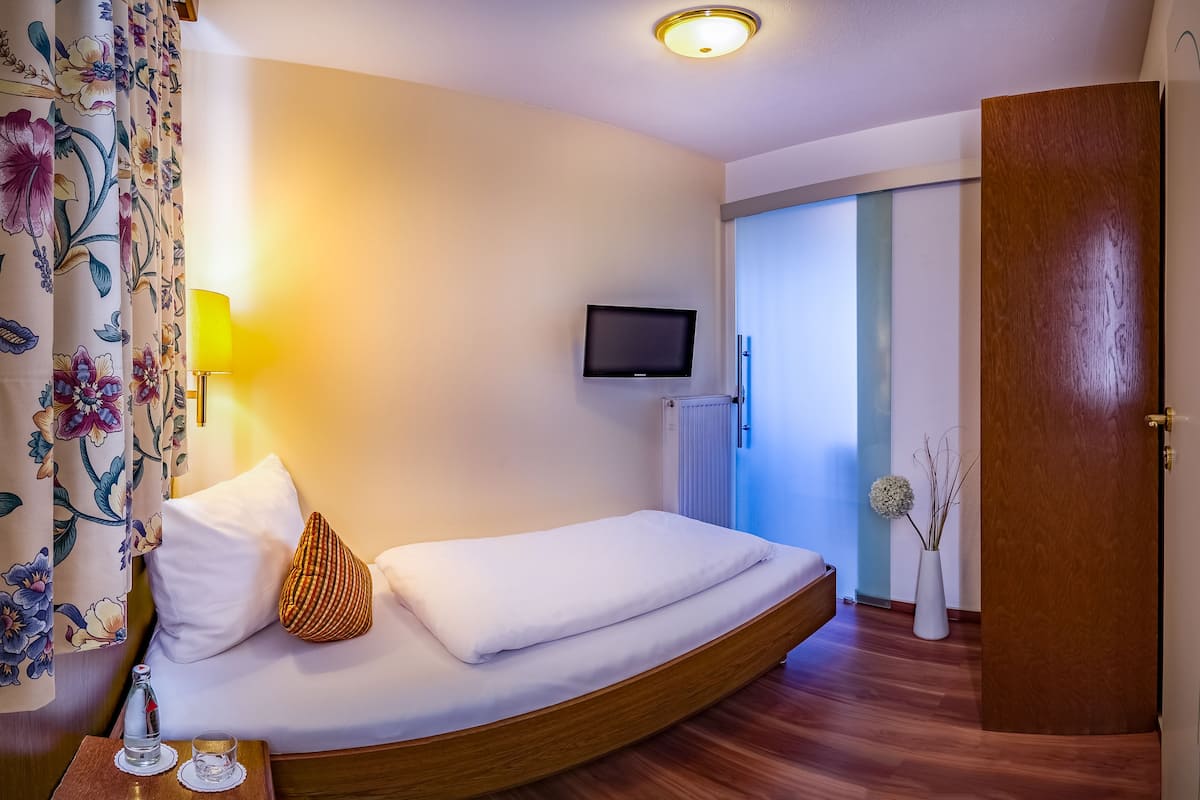 A modern hotel room with a curved bed, a flat-screen TV, a bedside lamp, and a floral curtain.