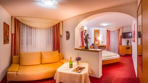A hotel room with a sofa, a small table with a bottle and glasses, a bed, a TV, and a mirror. - Hotel Kalenborner Hoehe (Kalenborn)