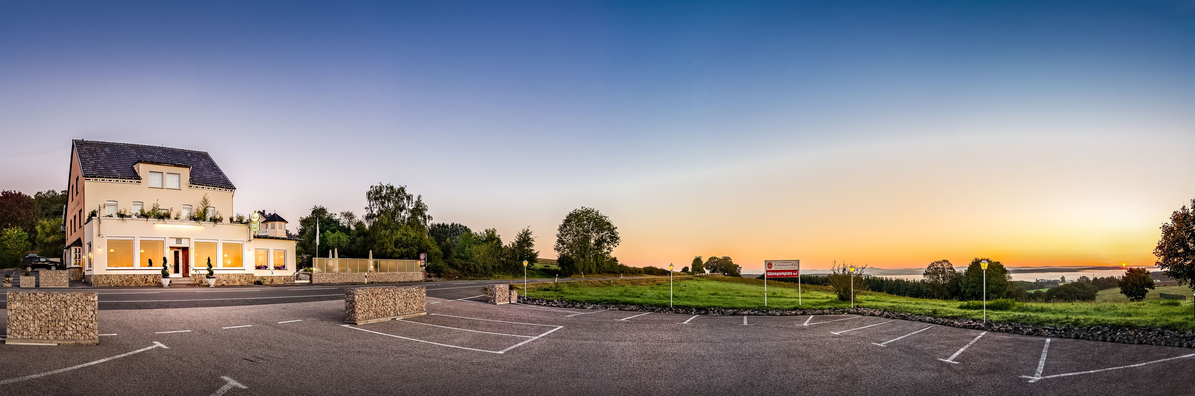 A hotel with a parking lot, stone walls, and a view of the sunset.