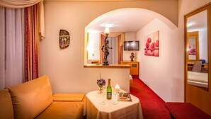 A hotel room with a sofa, a small table with a bottle and glasses, a TV, and a painting on the wall. - Hotel Kalenborner Hoehe (Kalenborn)