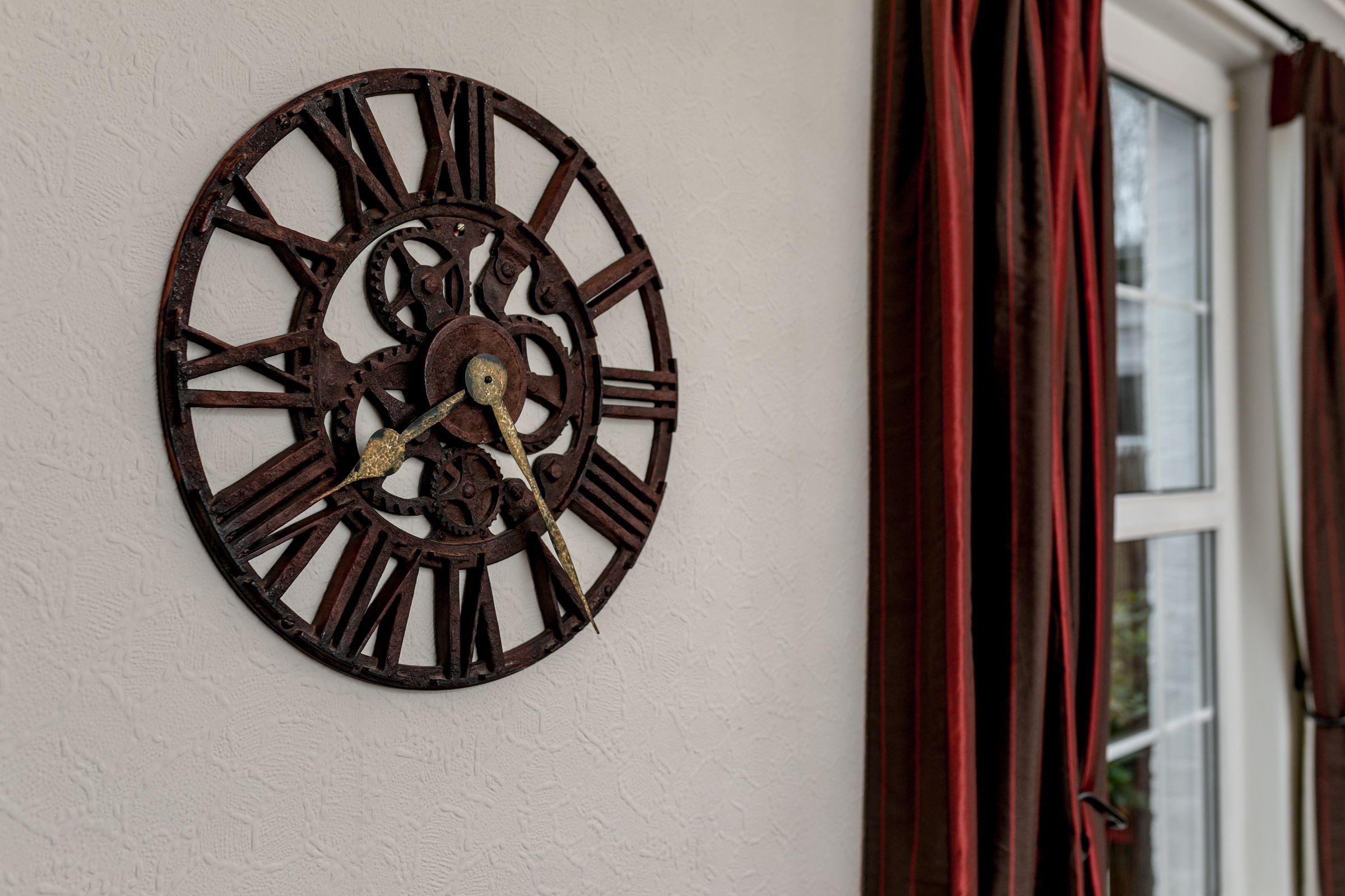 A wall-mounted clock with Roman numerals and a brass pendulum.