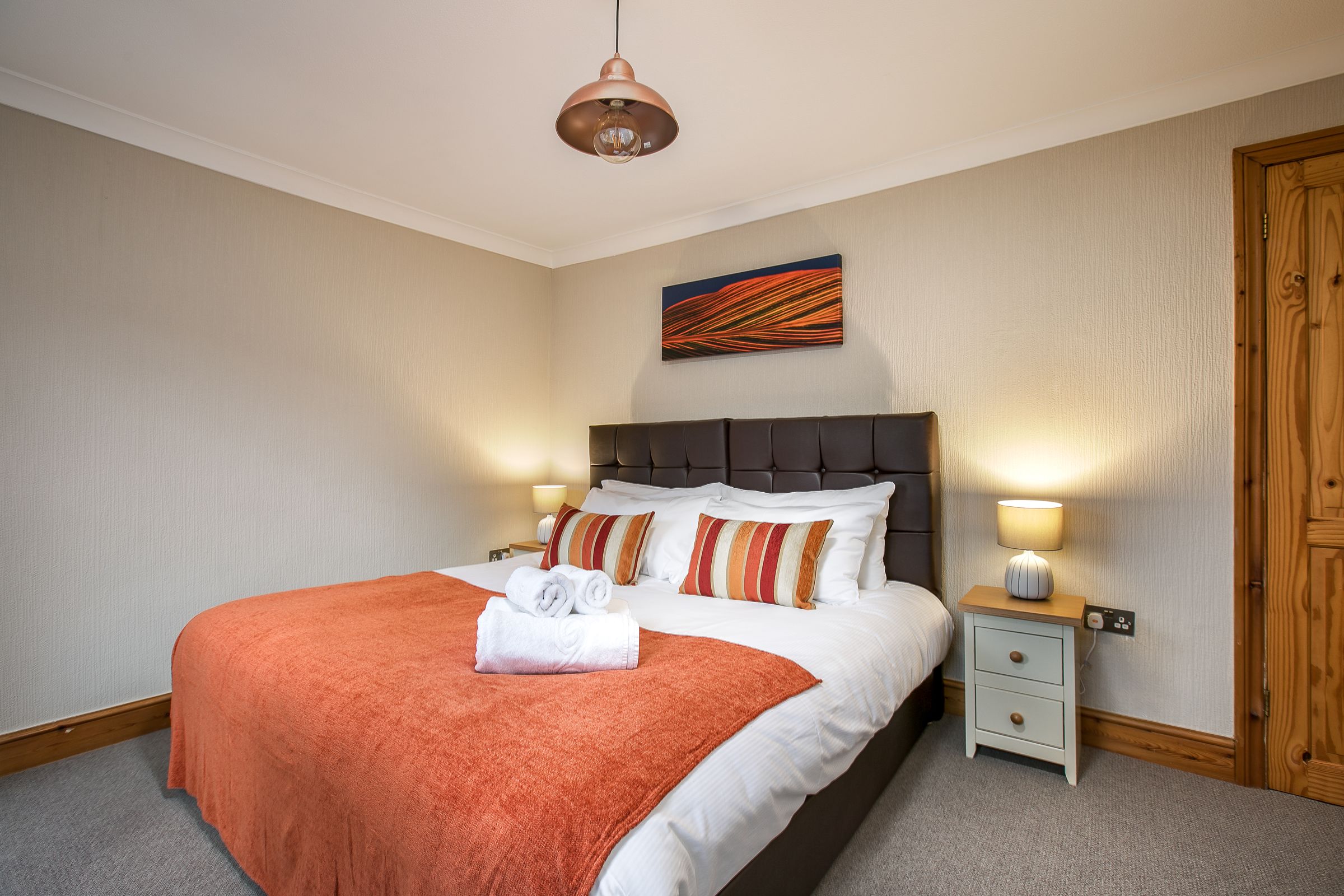 A neatly made bed with a red blanket, two bedside lamps, and a small bedside table with a lamp.