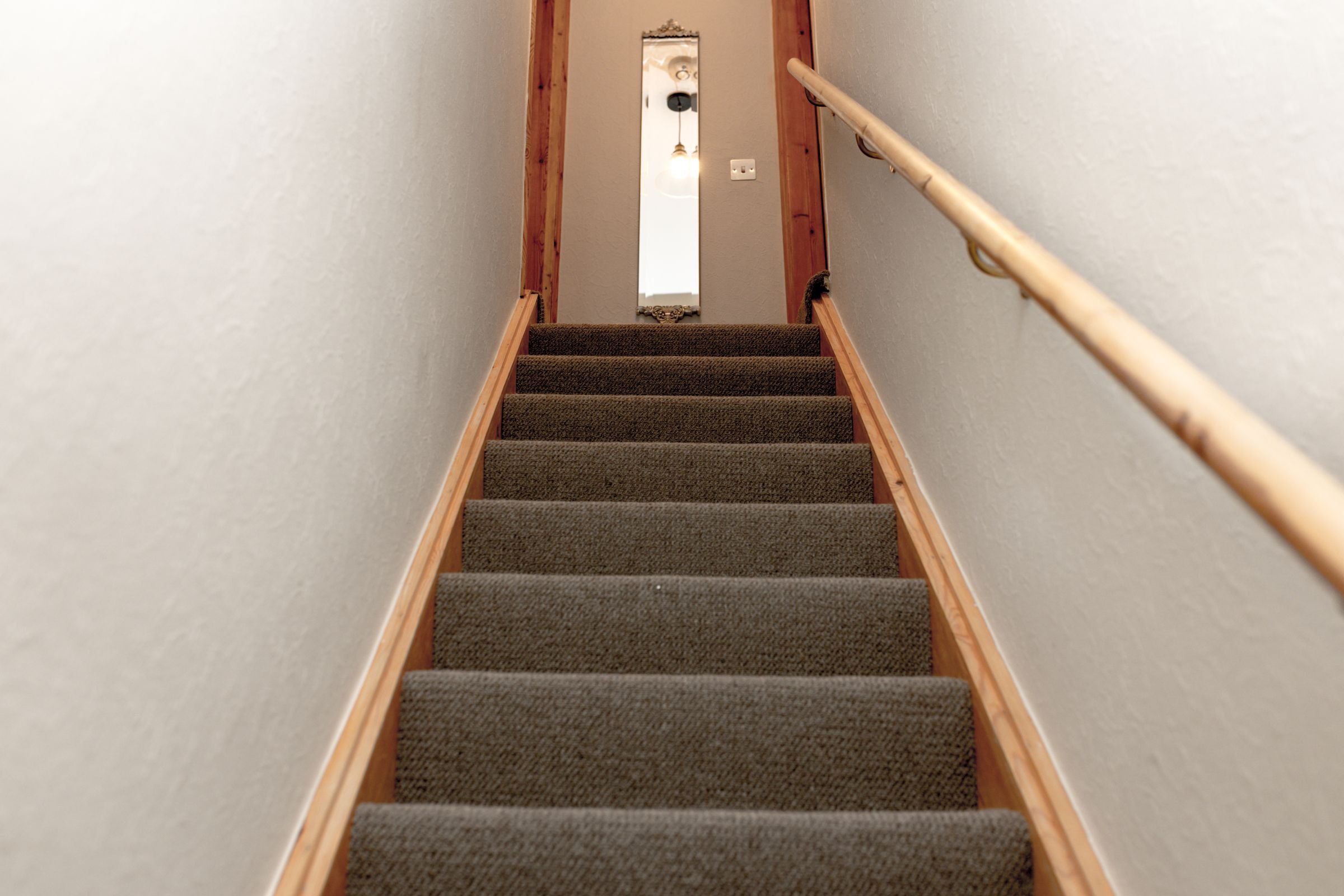 A staircase with carpeted steps and wooden handrails, leading to a door with a mirror and light fixture.