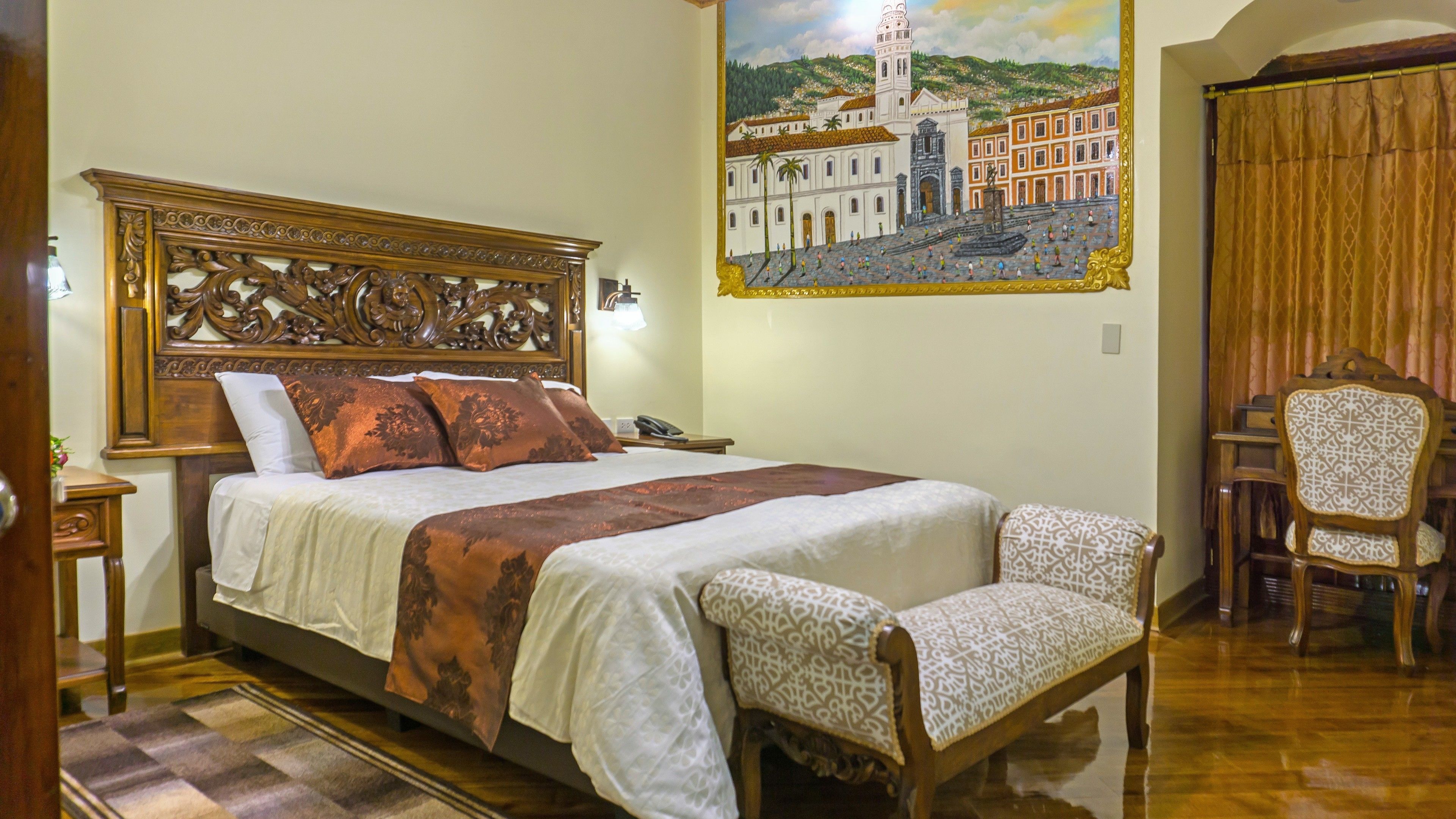 A hotel room with a large bed, a wooden headboard, a painting of a historical building, a wooden chair, and a small table.