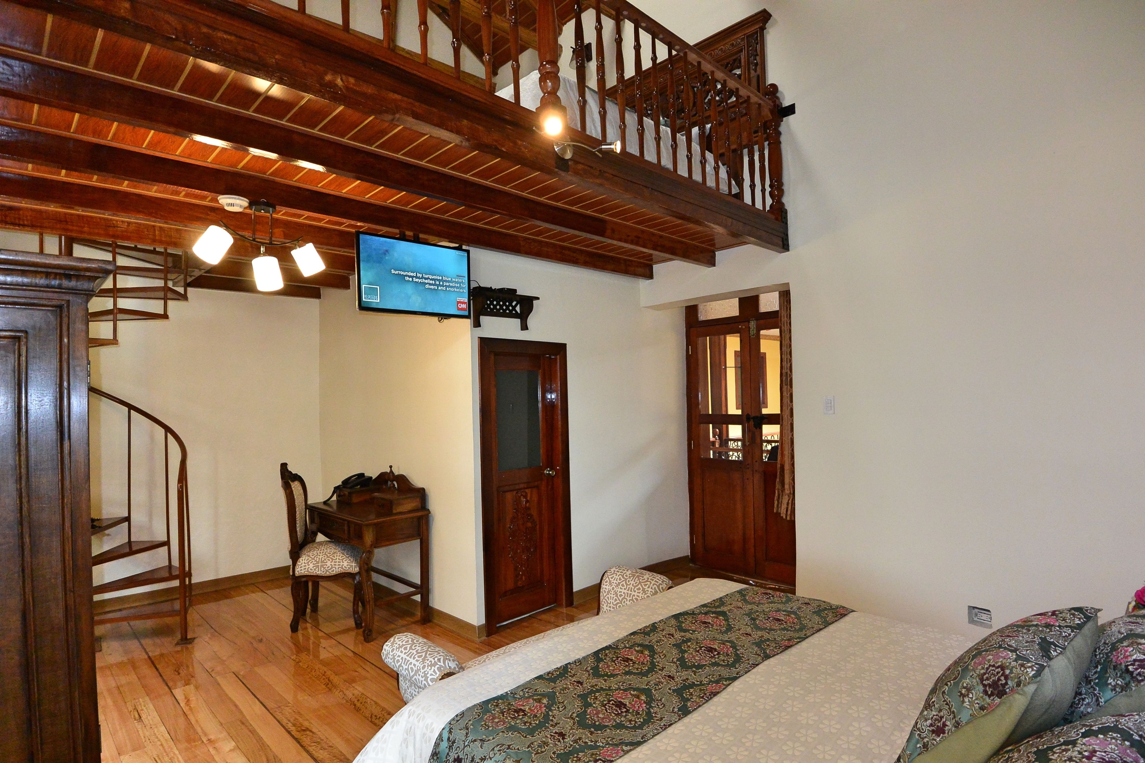 Quarto com escada de madeira, uma escrivaninha e cama com roupa de cama estampada.