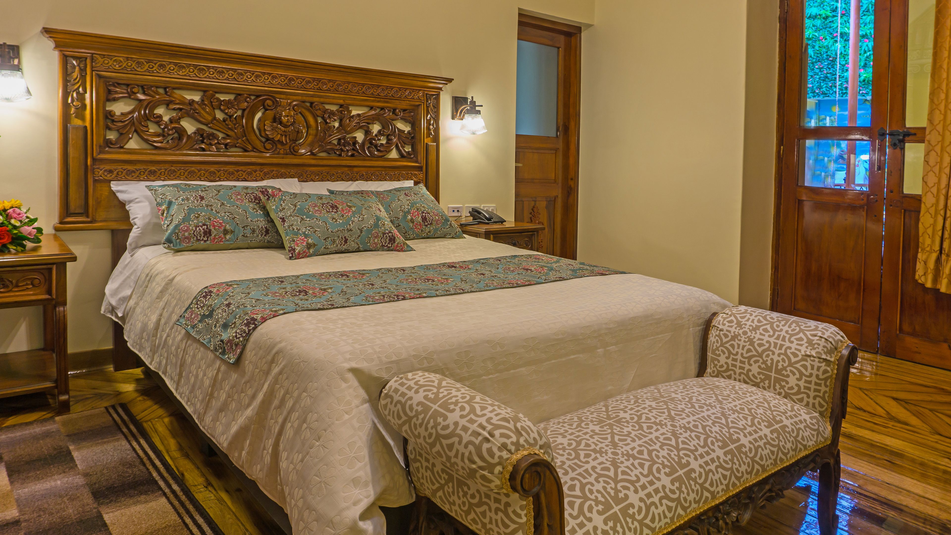 A neatly made bed with floral bedding, a wooden headboard, and a matching armchair.