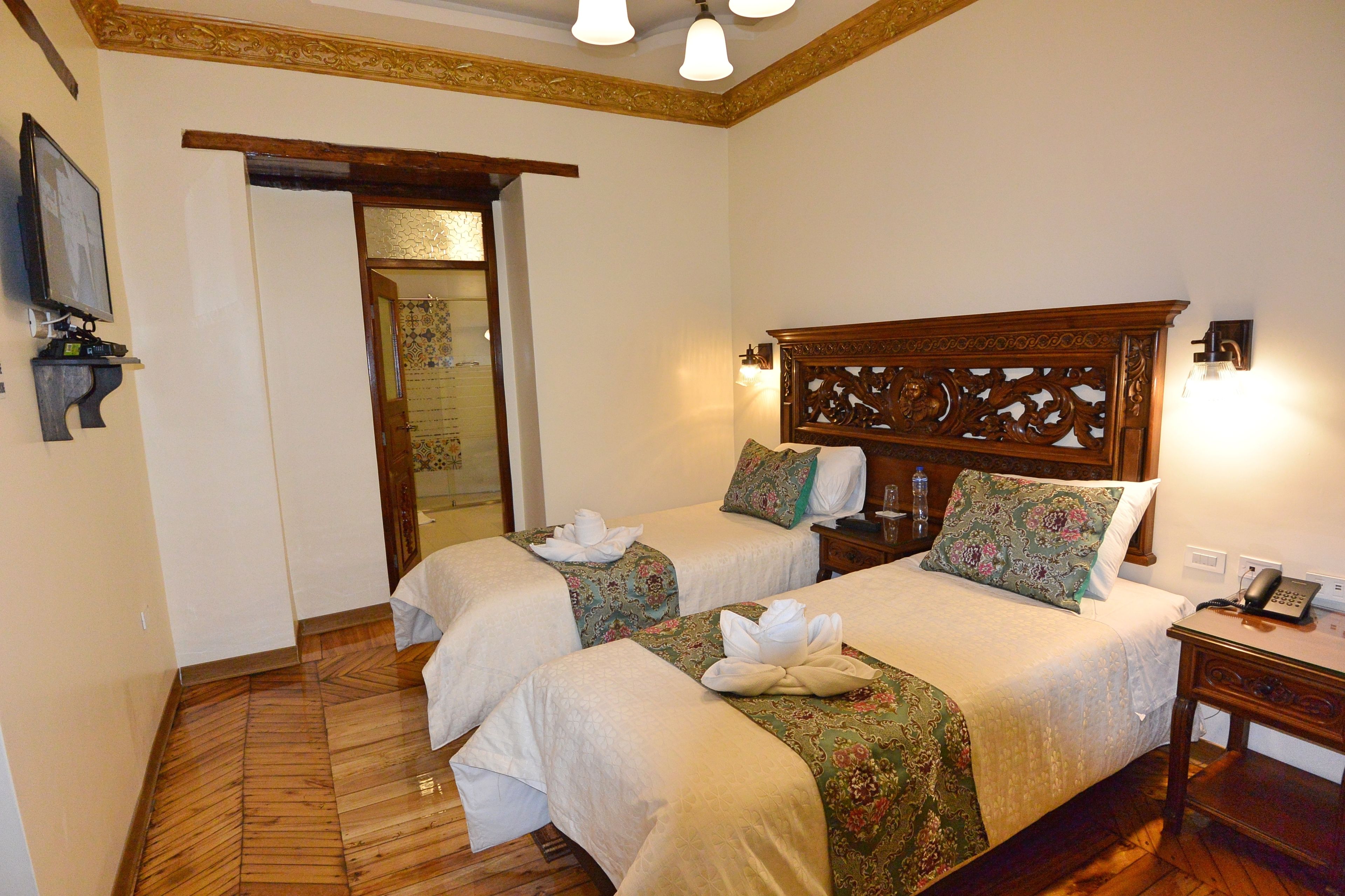 Une chambre d’hôtel avec deux lits, des têtes de lit en bois, une table de chevet avec un téléphone et un téléviseur fixé au mur.