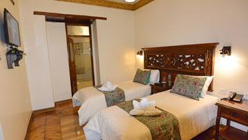 A hotel room with two beds, wooden headboards, a bedside table with a phone, and a wall-mounted TV.