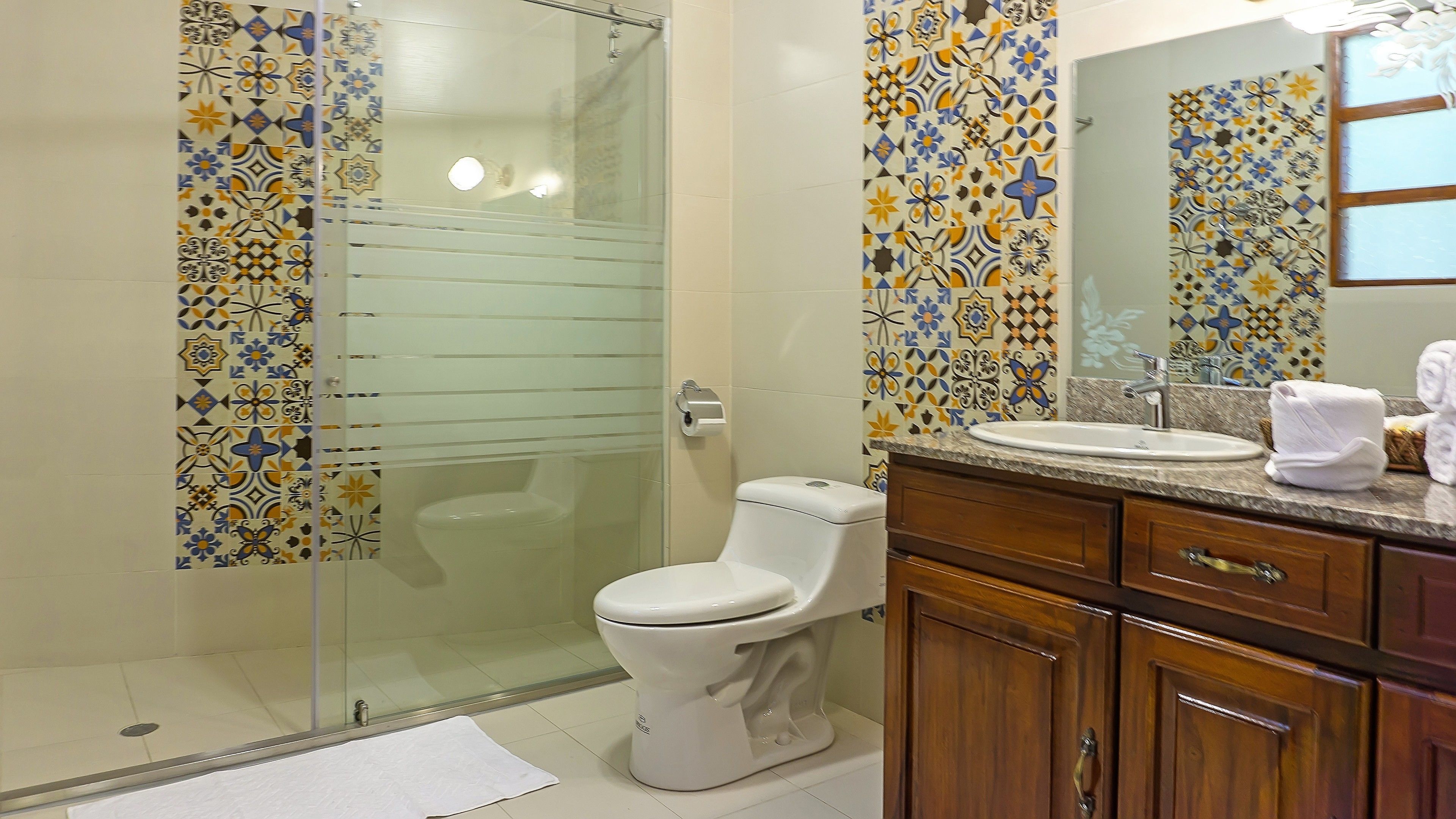 A bathroom with a glass shower enclosure, a toilet, a sink with a mirror, and wooden cabinets.