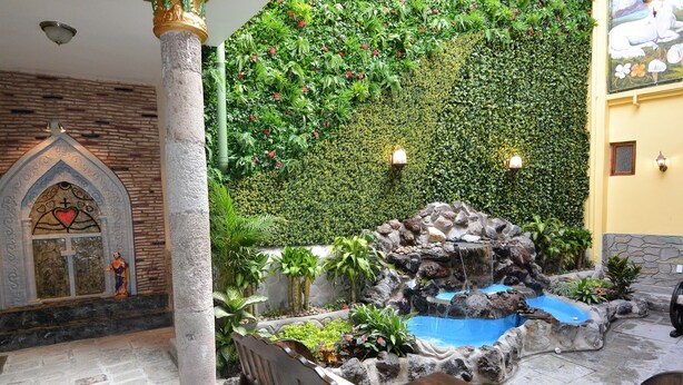 Un patio con un banco de piedra, una pequeña fuente y un muro cubierto de vegetación.