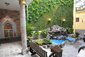 Un patio con un banco de piedra, una pequeña fuente y un muro cubierto de vegetación.